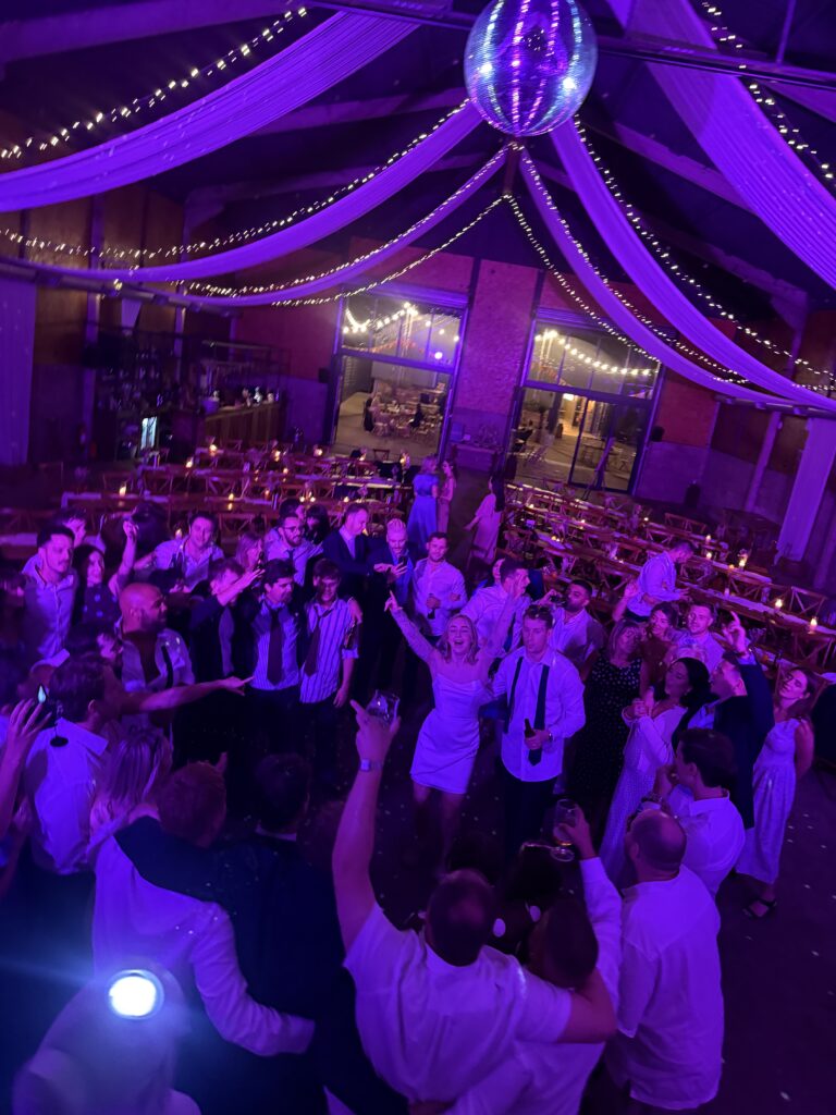 Packed Wedding dancegfloor with purple lighting and guests dancing